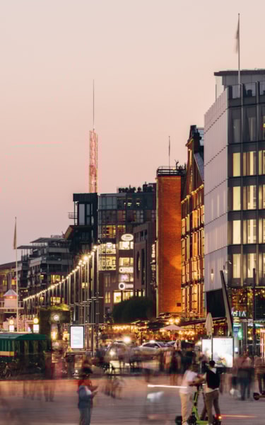 Evening at Aker Brygge with modern buildings, busy street life, and a boat docked by the waterfront.
