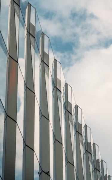 Close-up of a modern building with a glass facade reflecting the sky and clouds.