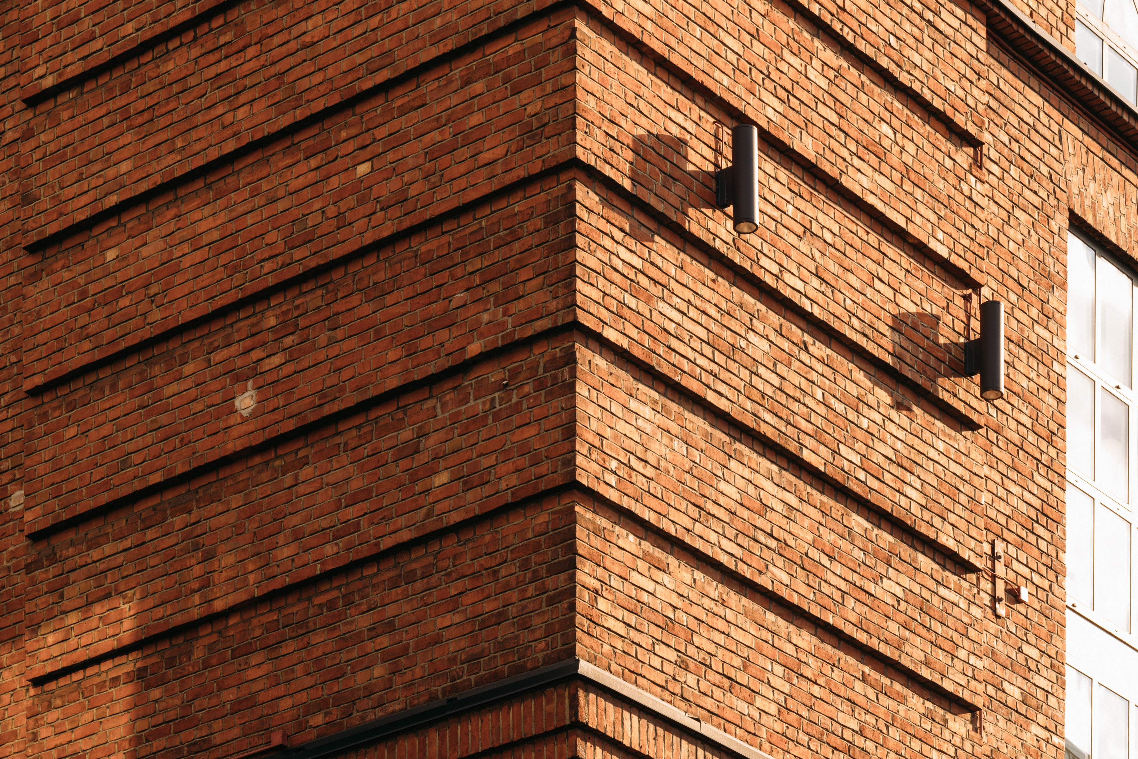 Nærbilde av hjørnet på en murbygning med sylindriske lysarmaturer og et vindu med flere ruter.