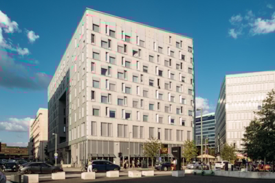 Full shot of the Diagonale building with a grid-like facade, surrounded by similar buildings, cars, and pedestrians on a sunny day.