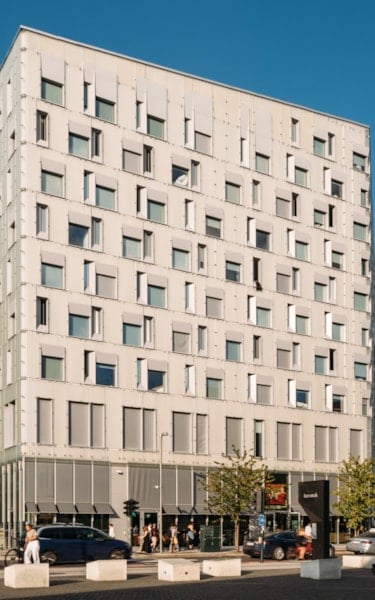 Full shot of the Diagonale building with a grid-like facade, surrounded by similar buildings, cars, and pedestrians on a sunny day.