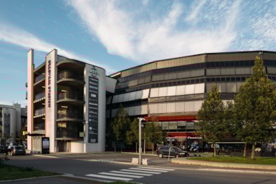 Full shot of Ullevaal Stadion with surrounding buildings, balconies, trees, parked cars, and a crosswalk in the foreground.
