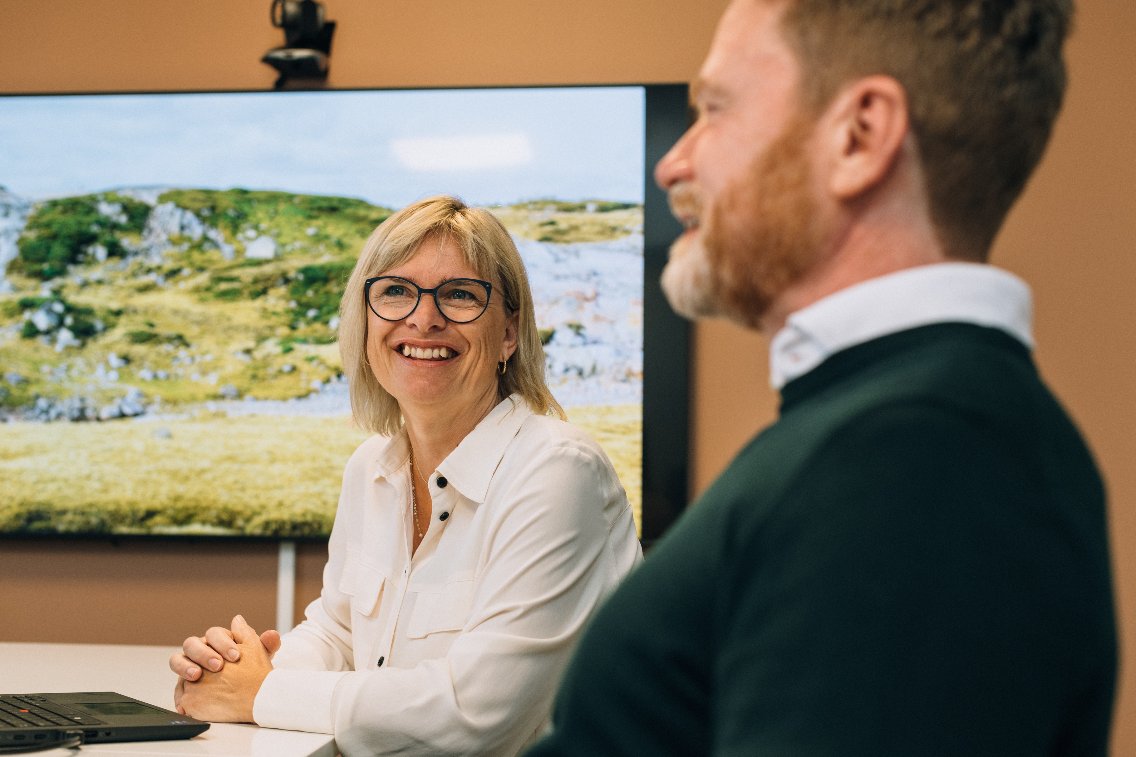 Two people sitting at a table, one using a laptop and the other with a notebook and pen.