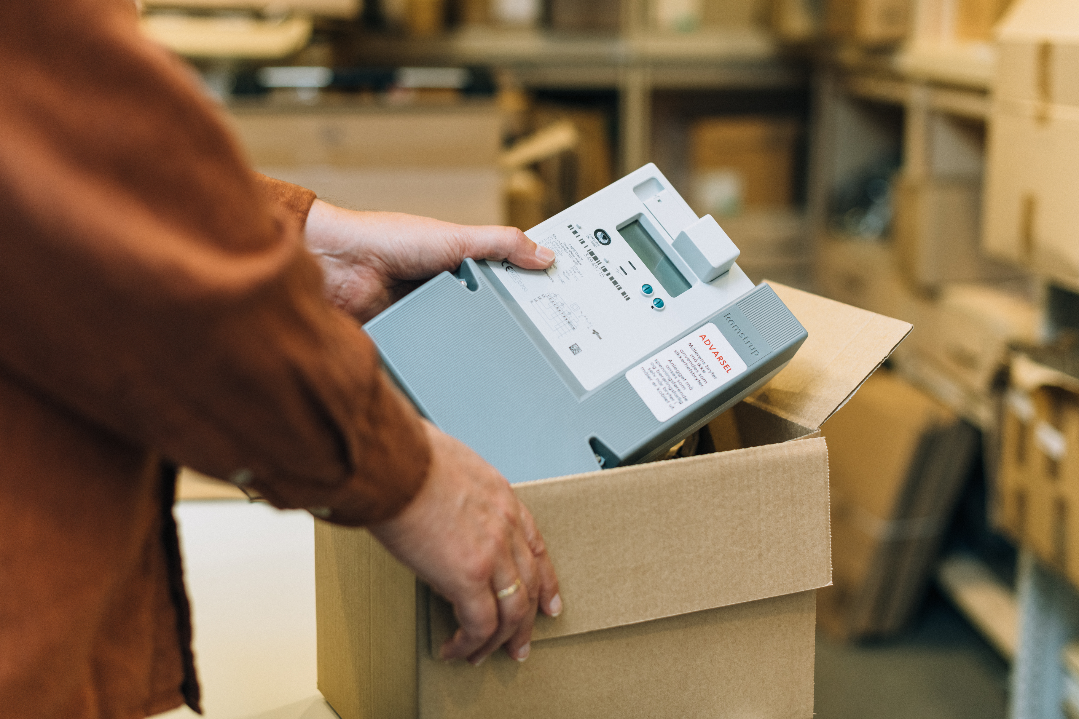 Nærbilde av en person som legger en strømmåler i en pappeske på et lager.